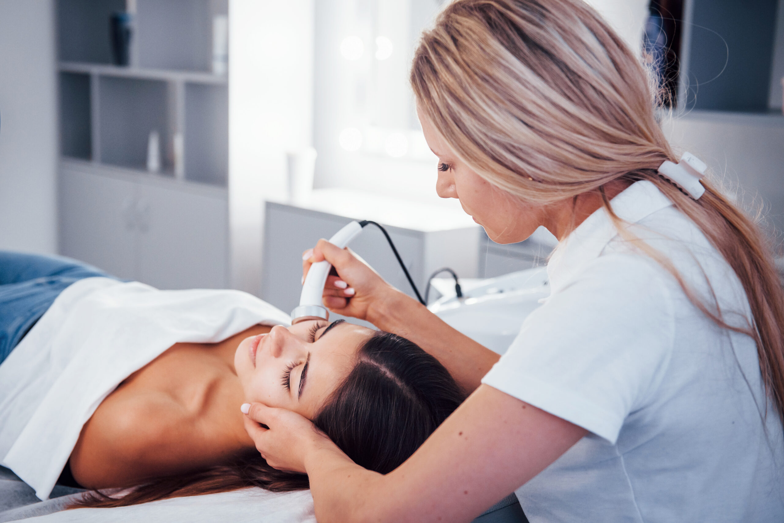 Woman lying down in spa salon and have face cleaning procedure by professional cosmetologist